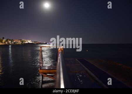 Dock and stairs to the sea on the harbour of Paphos, Cyprus, by night, under the moonlight in the sky with reflections on sea water Stock Photo