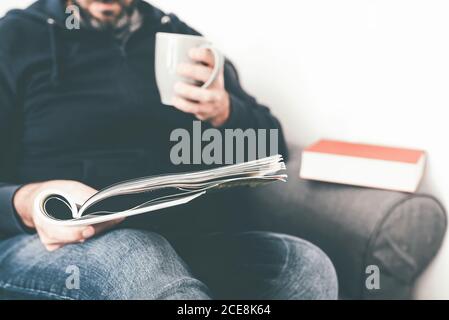 close-up of caucasian man reading magazine or journal on sofa while holding a cup of coffee Stock Photo