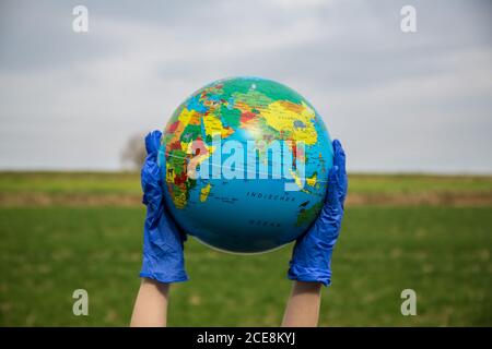Bamberg, Deutschland. 17th Mar, 2020. Bamberg, Germany March 17th, 2020: Symbolbilder - 2020 A globe in your hands with gloves, in front of a blue white sky and green landscape | usage worldwide Credit: dpa/Alamy Live News Stock Photo