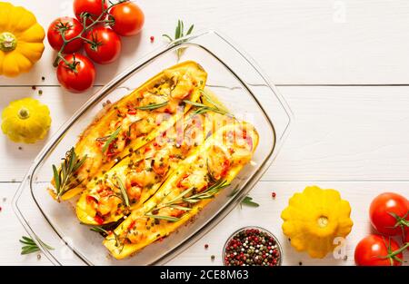 Stewed yellow zucchini with tomatoes and onions, cheese and herbs, carrots and spices, stuffed zucchini on a white wooden background Stock Photo