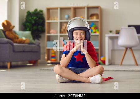 Boy in superhero costume and helmet sitting on floor and dreaming of being pilot Stock Photo