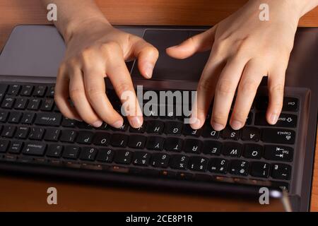 Human hands are typing text on a black laptop keyboard. Typesetter, freelancer and writer. Stock Photo
