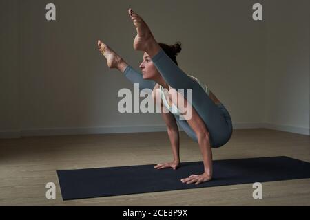 Side view of happy strong young female athlete in leggings balancing on arms while performing Firefly asana during yoga practice
