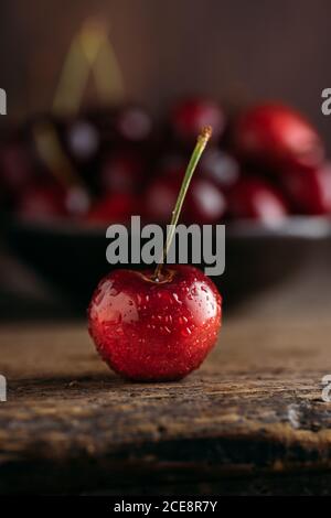 Close up view of cherry, on the background bowl full of fresh cherries on wooden table against dark background Stock Photo