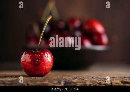 Close up view of cherry, on the background bowl full of fresh cherries on wooden table against dark background Stock Photo
