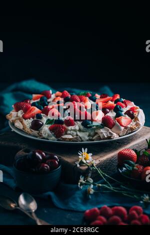 Delectable sweet meringue Pavlova cake with assorted fresh berries including strawberry and raspberry with cherry and blueberry served on table with berries and flowers Stock Photo