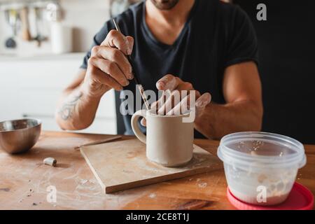 unrecognizable craftsman sitting at wooden table in workshop and making cup from clay Stock Photo