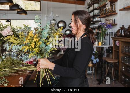 Side view of concentrated female designer arranging decorative blooming bouquets while working on order for event in creative floristry studio Stock Photo