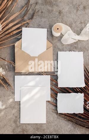 Tropical wedding invitation suite. Summer stationery mock-up scene. Blank greeting cards with dry palm leaves in sunlight. Shadow overlay. Grunge Stock Photo