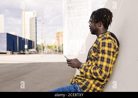 young african man with his phone leaning on a modern concrete structure at the city, concept of lifestyle and technology Stock Photo