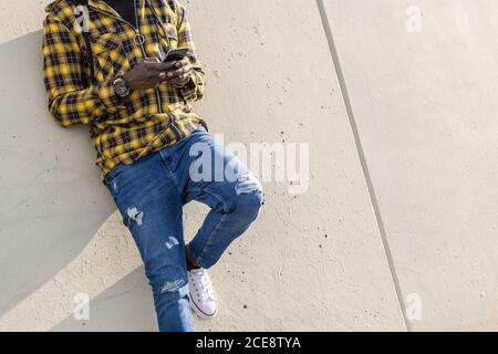 unrecognizable young african man writing a message on his phone leaning on a modern concrete structure, concept of lifestyle and technology Stock Photo