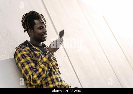 young black man recording a voice message on his phone leaning on a modern concrete structure, concept of lifestyle and technology Stock Photo