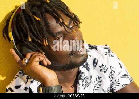 attractive young african man listening to and enjoying music with large headphones on yellow background, concept of technology and lifestyle, copy space for text Stock Photo