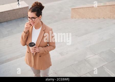 Above view of account manager in jacket drinking coffee and talking to client by phone being on move Stock Photo