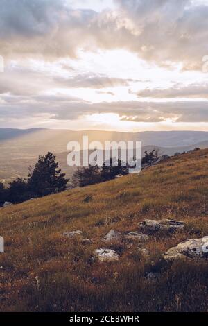 Majestic scenery of highland area under breathtaking sunset sky with sun shining through clouds in fall Stock Photo