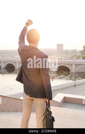 Rear view of young business student standing with raised arm and looking at city, he ready to be successful Stock Photo
