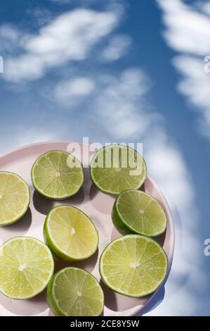 From above of halves of ripe limes arranged on pink plate on blue background with tree shadows Stock Photo
