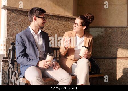 Creative colleagues sitting with coffee cups on bench and discussing business ideas during coffee break Stock Photo