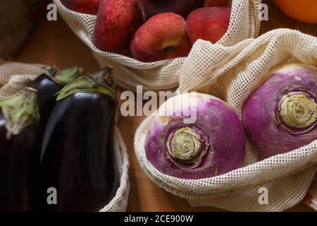 Assorted vegetables and fruits in paper and mesh cotton fabric reusable packages placed on wooden table in kitchen Stock Photo