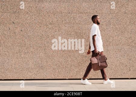 Side view of modern bearded African-American businessman with portfolio walking over street Stock Photo