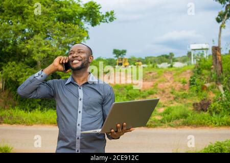 Young African male using a laptop and smartphone on his farmland Stock Photo