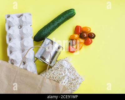 Food in a paper bag: eggs, canned food and oat groats on a yellow background Stock Photo