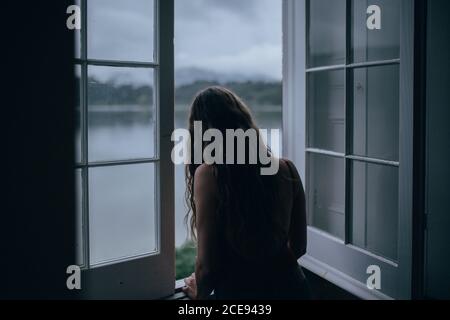 Woman looking through window of room Stock Photo