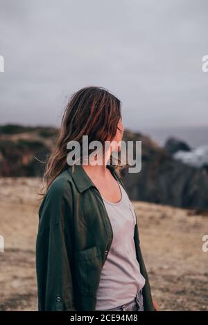 Side view of casual Woman turning away from camera while standing on coast of Vicentina in clouds, Portugal Stock Photo