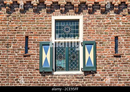 Hattem, The Netherlands, July 31, 2020: part of the facade of the Dijkpoort (dike gate), with a small stained glass window with wooden shutters in a b Stock Photo