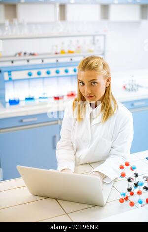 Cute female researcher in white lab coat using laptop while working in the laboratory Stock Photo