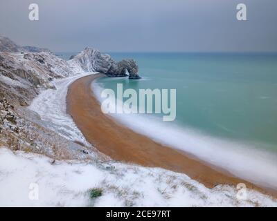 The rock arch of Durdle Door covered in snow. Stock Photo