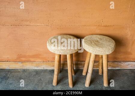 Two handmade wooden chairs with wicker straw pillows on background of red terracotta wall with decorative plaster. Moroccan rustic interior and furniture design. Stock Photo