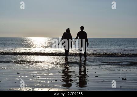 Majestic shot of a silhouette of a young couple walking barefoot on sandy coastline Stock Photo