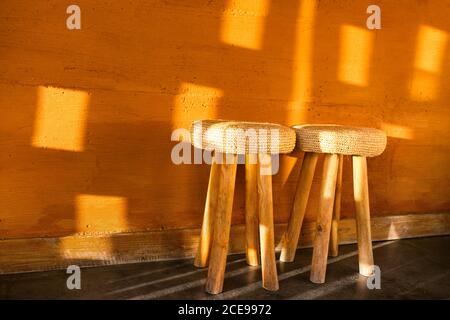 Two handmade wooden chairs with wicker straw pillows on background of red terracotta wall with decorative plaster. Moroccan rustic interior and furniture design. Warm sun light. Stock Photo