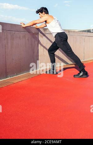 rear view of a sportsman stretching legs on a concrete wall, concept of urban sport and healthy lifestyle, copy space for text, vertical photo Stock Photo