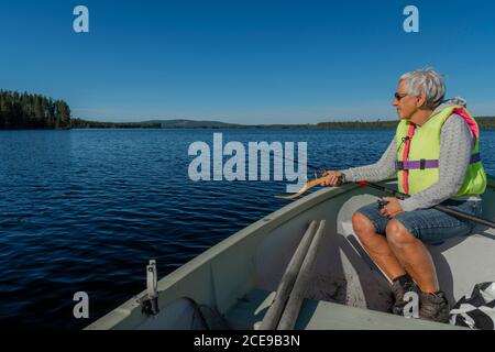 Retired women in a small boat on a lake fishing with old equipment, blue sky and horizon in background, picture from Vasternorrland Sweden. Stock Photo