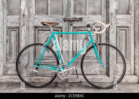 Vintage seventies light blue racing bicycle with leather saddle in front of old black and white wooden doors Stock Photo