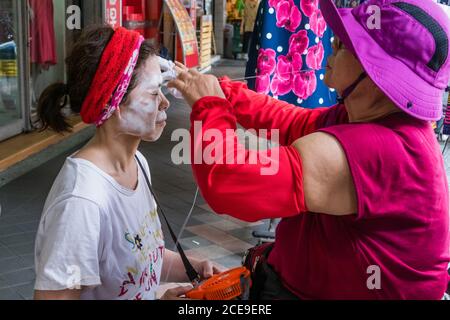 NEW TAIPEI CITY, TAIWAN - JULY 23: Unidentified woman gets a traditional string facial by a beautician on the sidewalk. Stock Photo