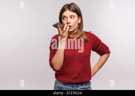 Brunette woman in shaggy sweater talking to mobile phone, using virtual assistant, ai intelligent technology, digital voice application, audio message Stock Photo