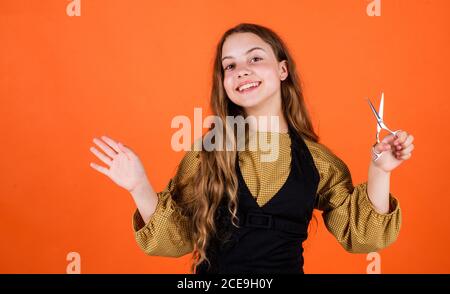 child with scissors wants to cut hair. girl in hairdressing salon. teenager cutting hair. Cute girl cutting hair to herself with scissors. kid is trimmed in the hairdressers. Form follows you. Stock Photo