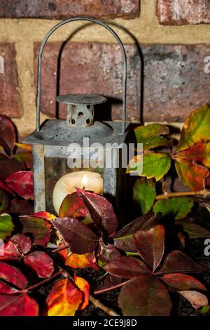 An old weathered candle holder shaped liked a lantern surrounded by the colorful autumn leaves of a Virginia creeper, against a brick wall Stock Photo