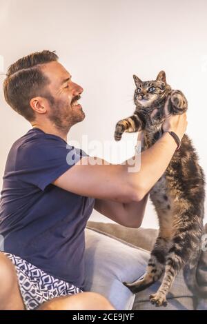 Young Caucasian man in a blue T-shirt and shorts playing at home with his beautiful cat Stock Photo