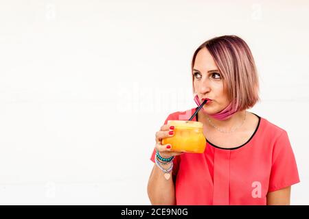 Cool woman drinks a glass of freshly squeezed orange juice during coronavirus outbreak - She drinks thirst-quenching orange juice for healthy lifestyl Stock Photo