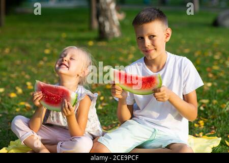 To cute kids lttle boy and girl eating juicy watermelon in the autumn park meadow Stock Photo