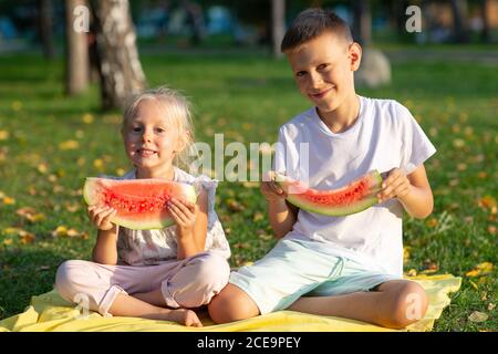 To cute kids lttle boy and girl eating juicy watermelon in the autumn park meadow Stock Photo