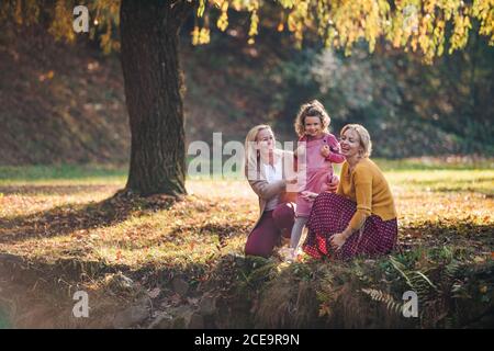 Small girl with mother and grandmother resting in autumn forest. Stock Photo