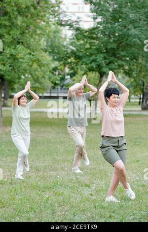 Qigong coach standing with crossed legs and teaching seniors to do balance exercise in park Stock Photo