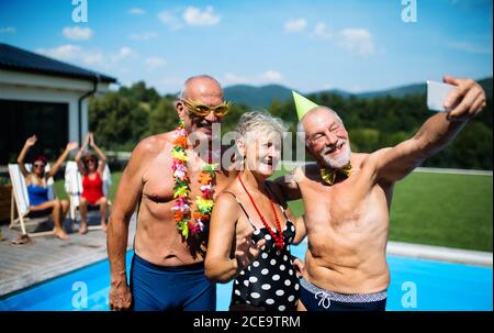 Group of cheerful seniors by swimming pool outdoors in backyard, taking selfie.