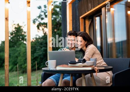 Young couple with laptop outdoors, weekend away in container house in countryside. Stock Photo
