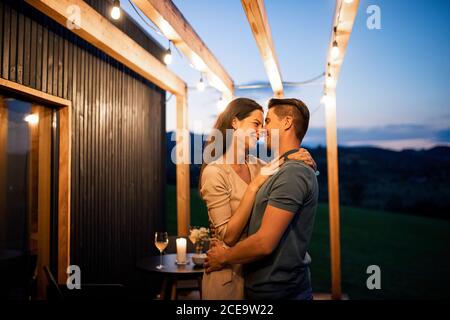 Young couple dancing outdoors at dusk, weekend away in container house in countryside. Stock Photo